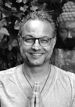 Thomas Lücke mit gefalteten Händen vor einer Buddha-Statue
